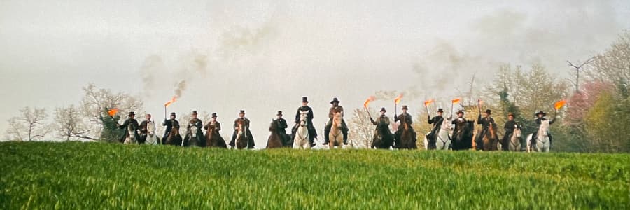 A line of men on horseback holding torches along the horizon of a field.