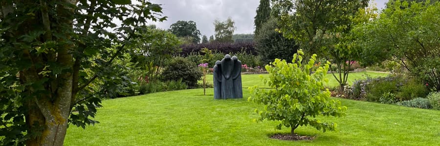 Three distant dark figures on the lawn of a bright garden.